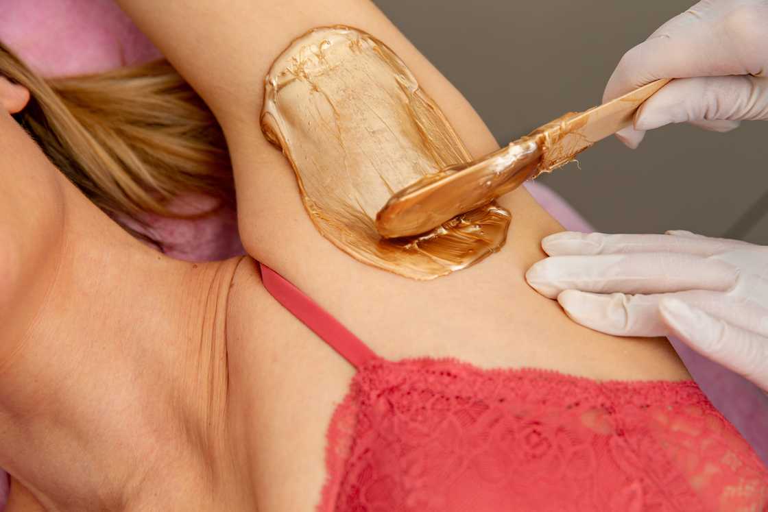 A beautician applies wax on a woman's armpit