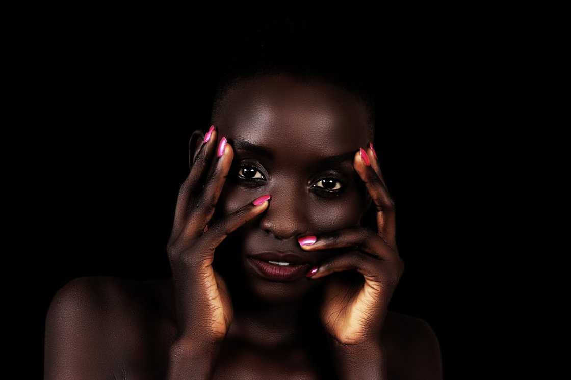 A close-up portrait of a woman against a dark background, hands framing her face. A close-up portrait of a woman against a dark background, hands framing her face.