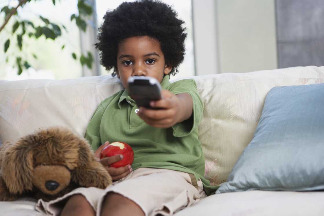 A kid holds a tv remote and an apple