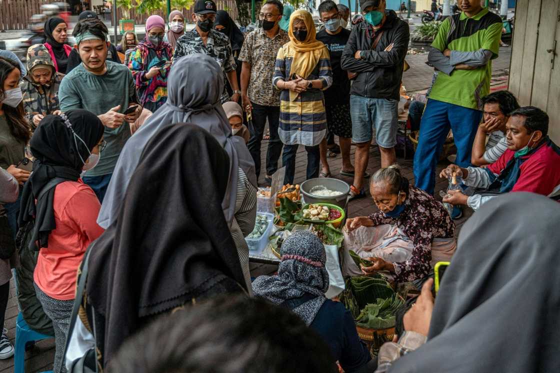 As the morning twilight approaches in an Indonesian city famed for its street food scene, customers gather around Mbah Satinem as she prepares her famous lupis