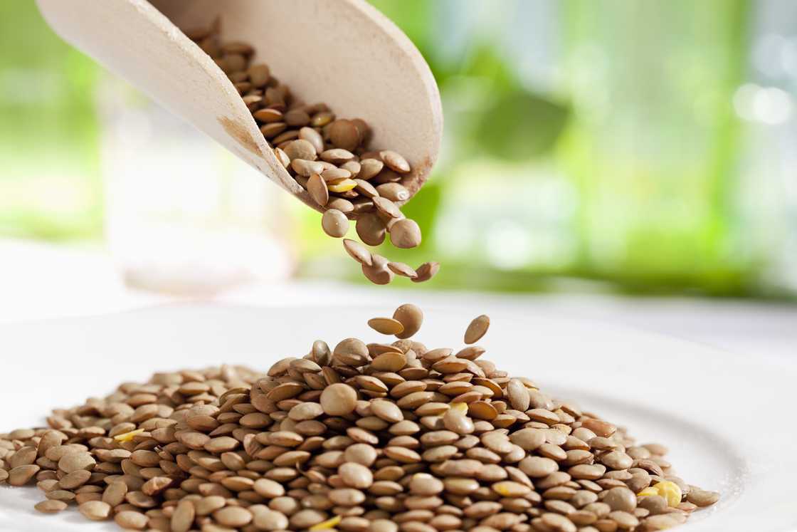 Lentils pouring from wooden scoop, close up