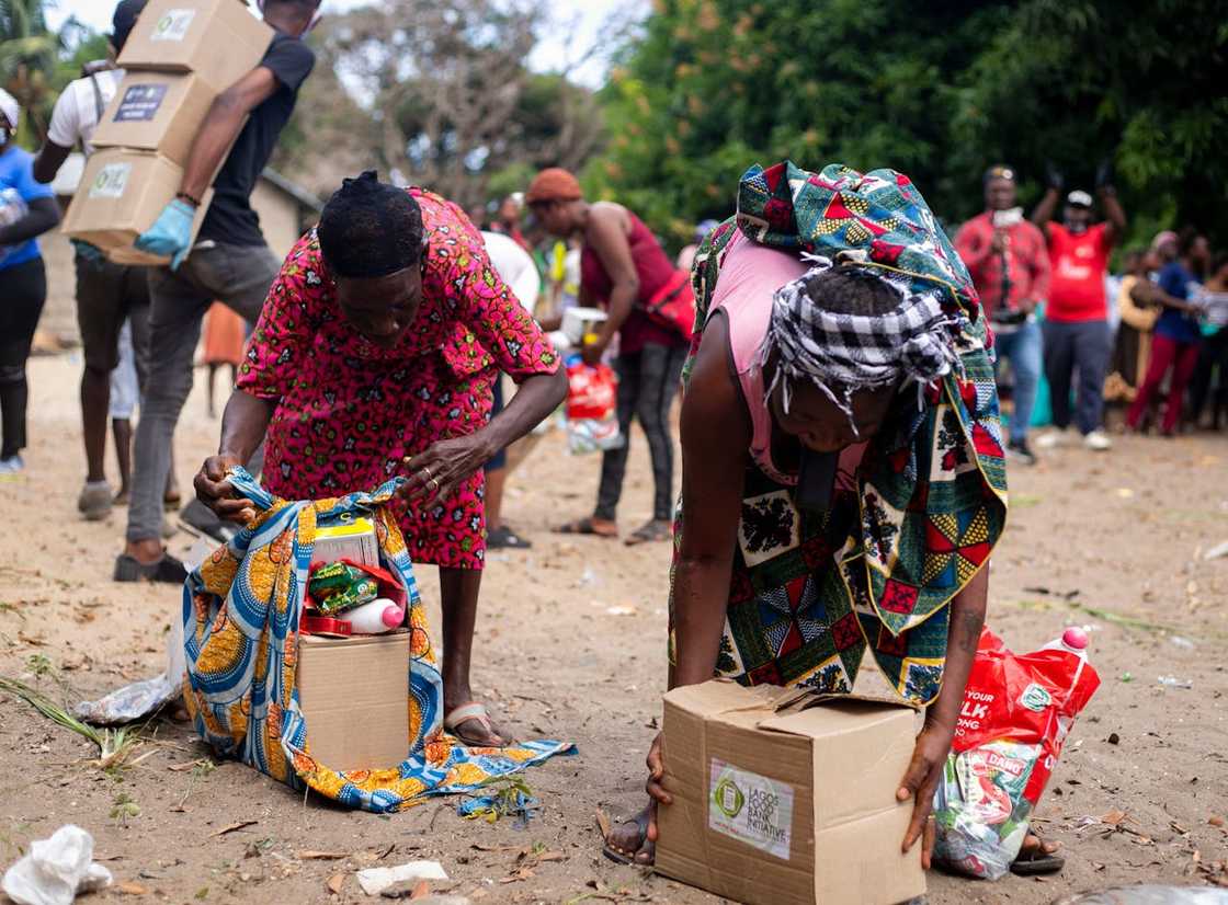 Women bend to collect relief supplies from cardboard boxes.