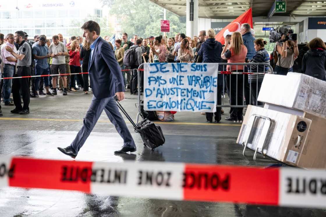 A traveller walks by a picket line where a sign reads 'I am not an economic adjustment variable' A traveller walks by a picket line where a sign reads 'I am not an economic adjustment variable'