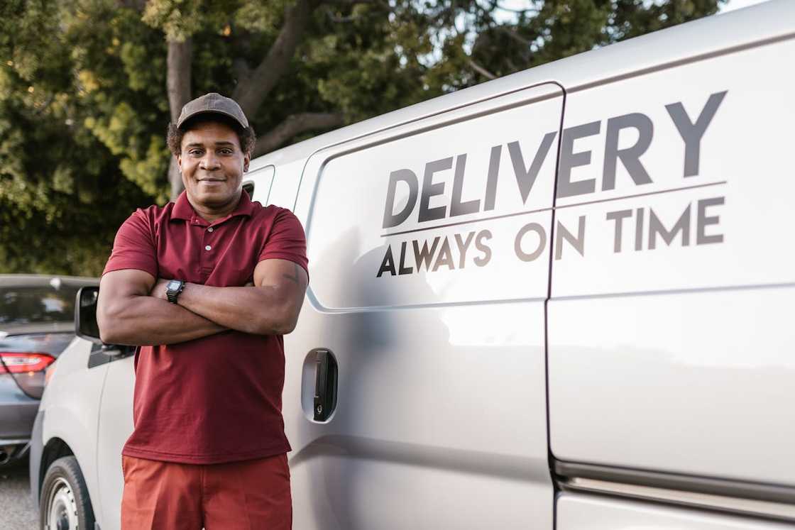 A delivery worker stands confidently beside a van with delivery signage. A delivery worker stands confidently beside a van with delivery signage.