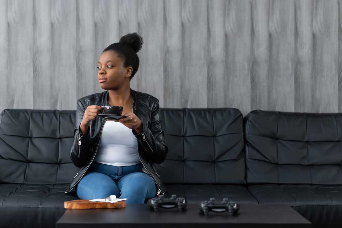 Young calm black woman relaxing sitting on black sofa