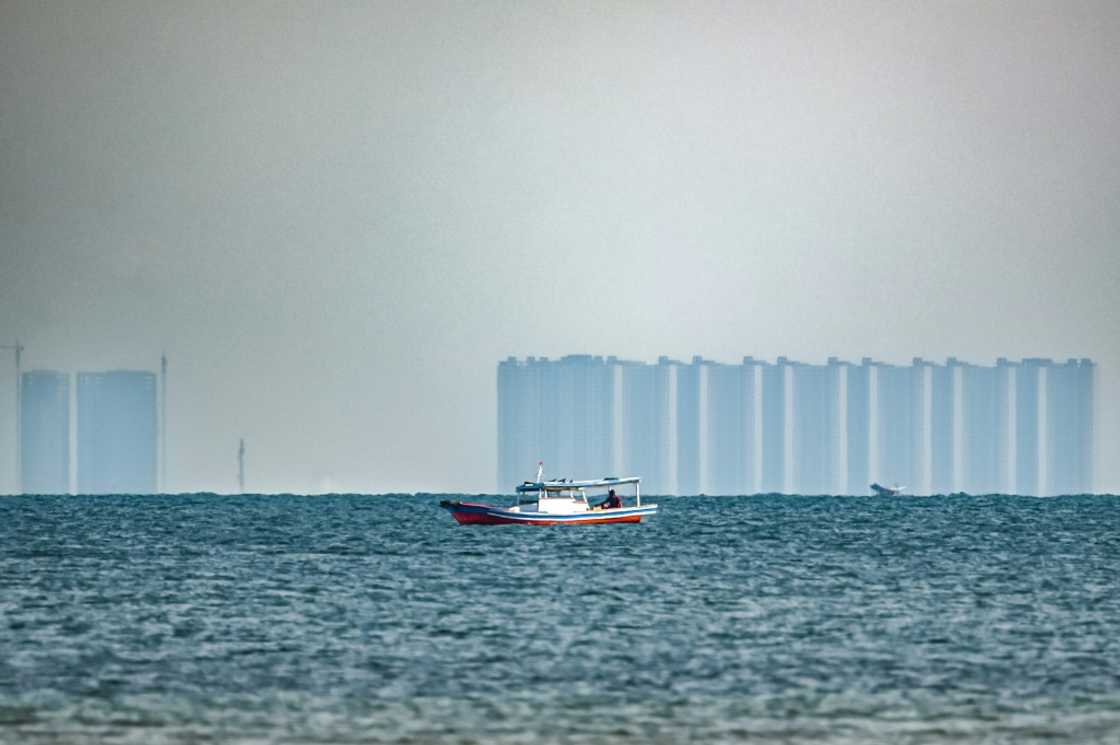 A man fishes off Pari, as buildings located in the northern part of nearby Jakarta are seen in the distance