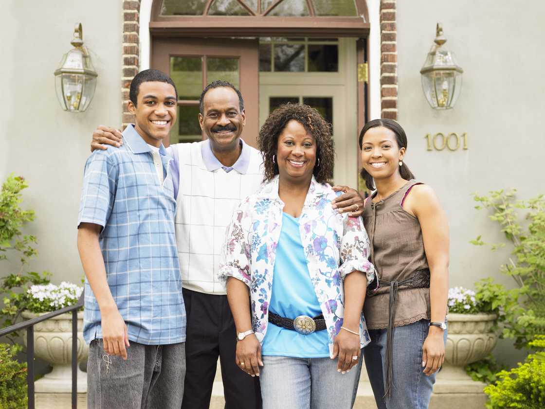 Four people stand smiling in front of a house. Four people stand smiling in front of a house.