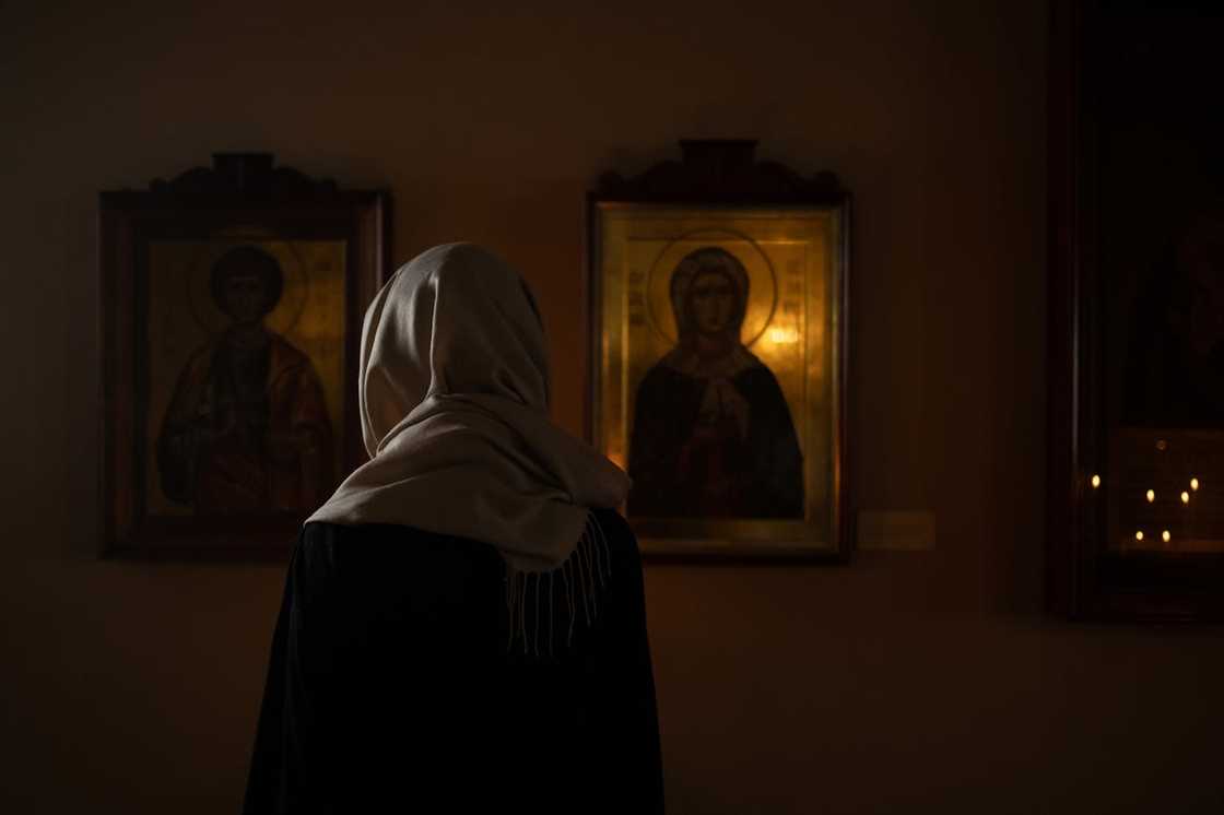 A woman wearing a headscarf standing in a dimly lit chapel, facing religious icons.