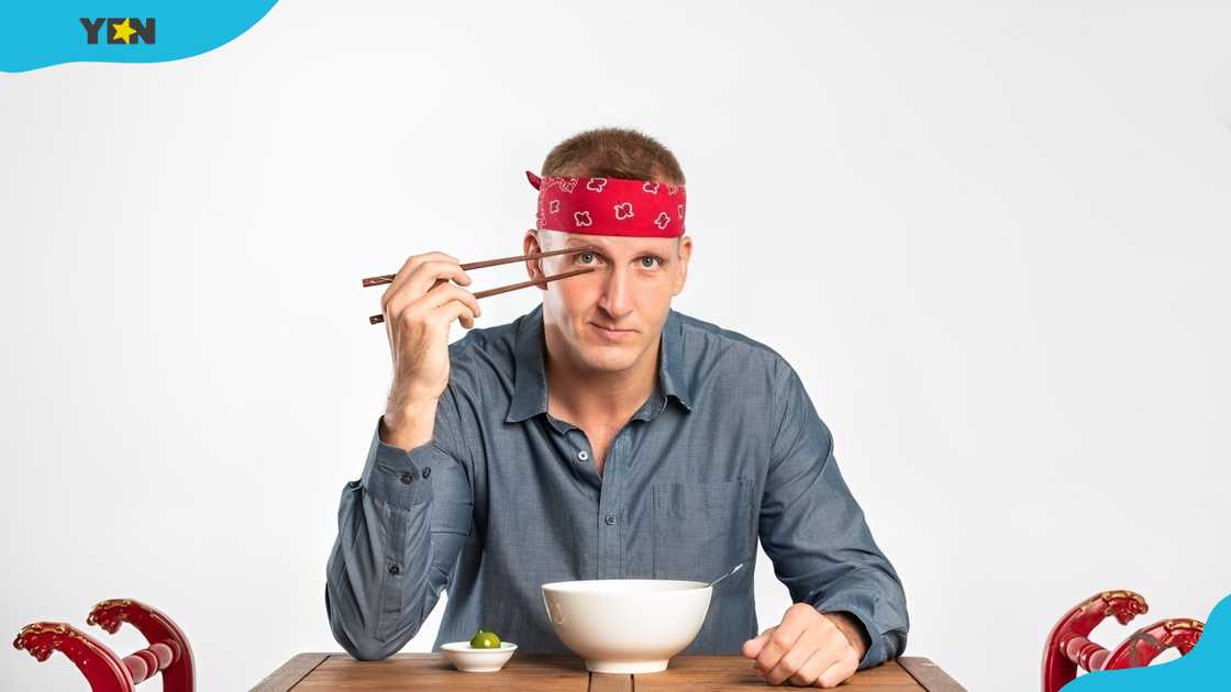 Will Sonbuchner, in a red bandana and a blue shirt, playfully holds chopsticks at a table with food. Will Sonbuchner, in a red bandana and a blue shirt, playfully holds chopsticks at a table with food.