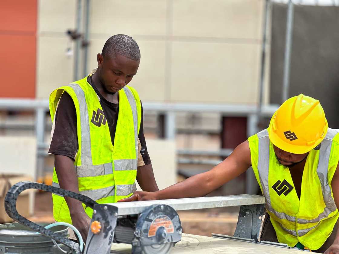 Two workers operate a tile-cutting machine at a construction site.
