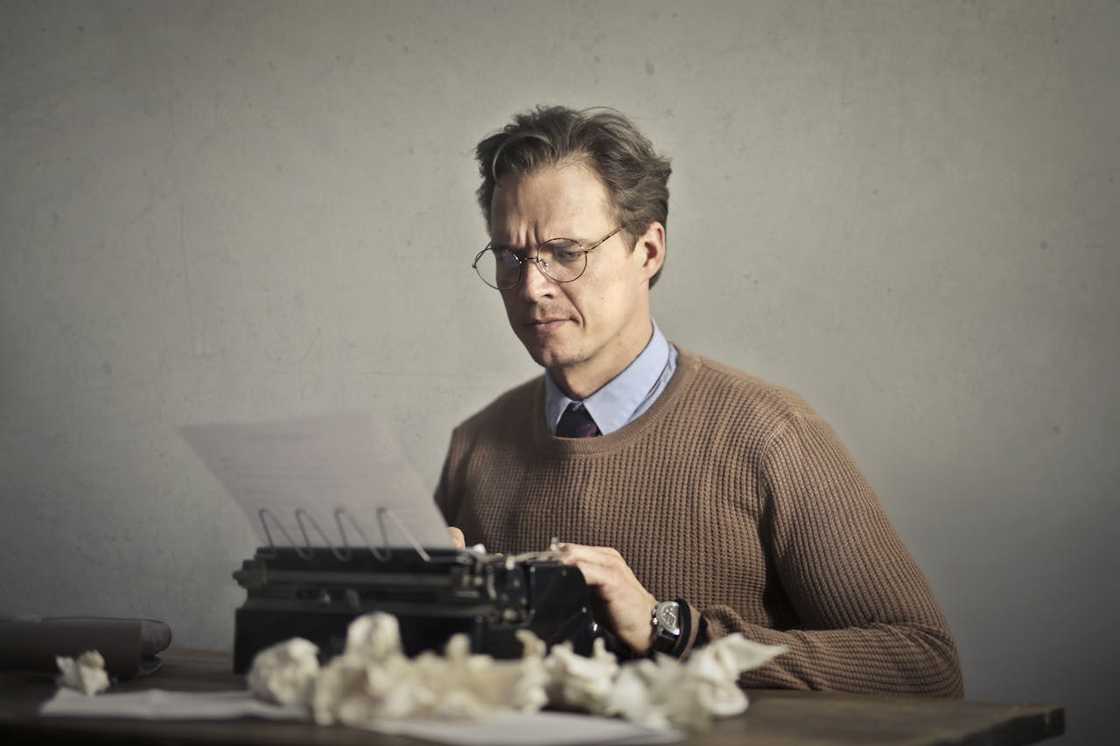 An adult frowned male writer working on a typewriter at home An adult frowned male writer working on a typewriter at home