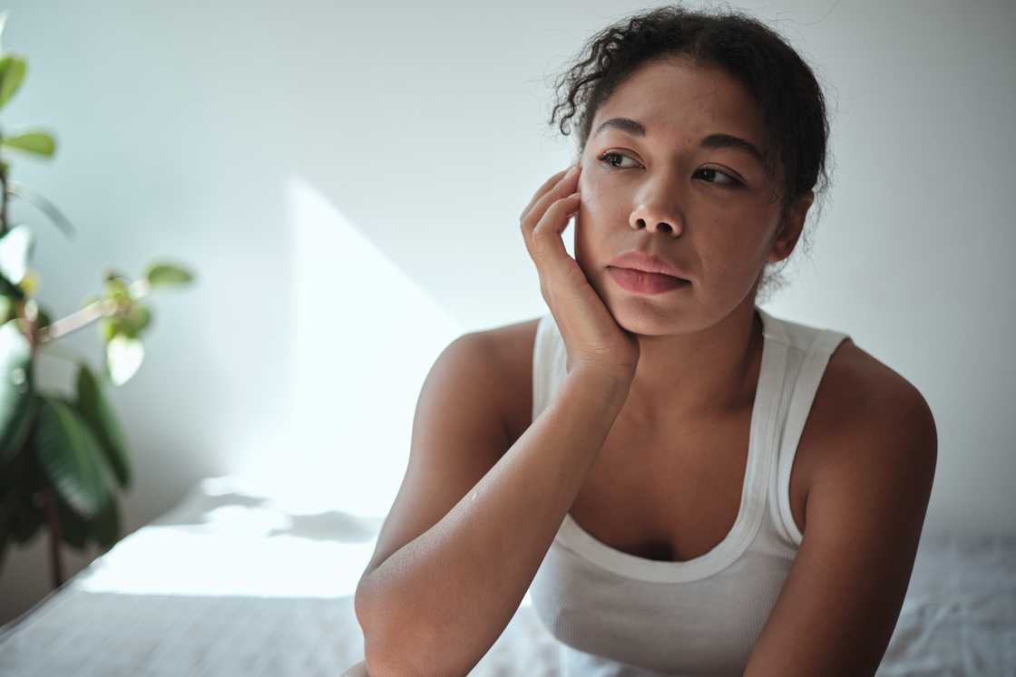 A sad woman sitting on bed waking up tired