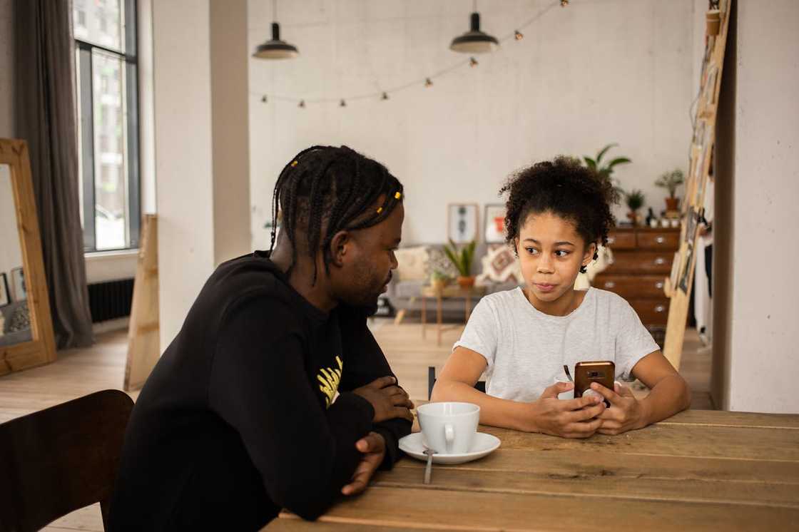 A father and daughter sitting at a table while talking. A father and daughter sitting at a table while talking.