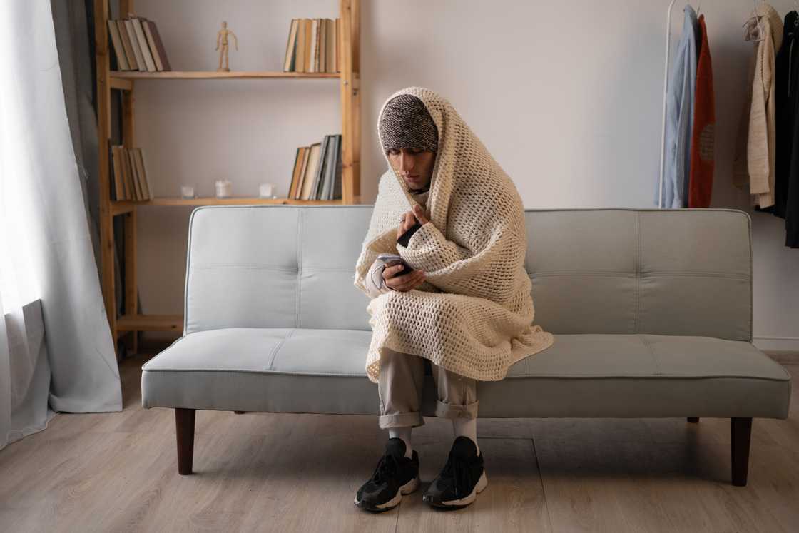 A man in a hoodie sitting alone with a blanket.