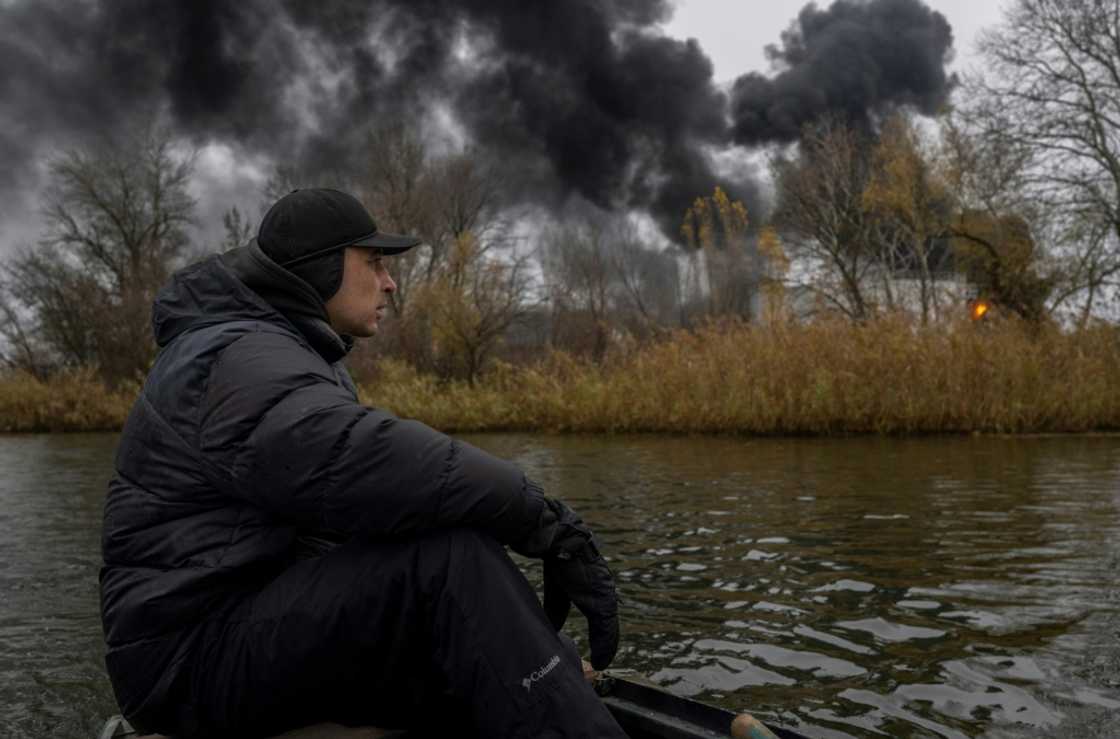 A fisherman sails his boat on the Dnipro River as black smoke rises from an oil depot in Kherson, on November 20, 2022, amid the Russian invasion of Ukraine A fisherman sails his boat on the Dnipro River as black smoke rises from an oil depot in Kherson, on November 20, 2022, amid the Russian invasion of Ukraine