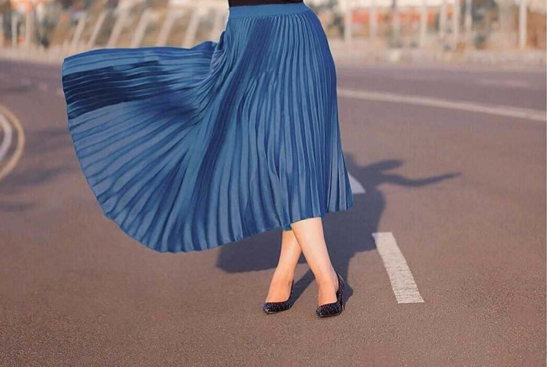A woman stands on the road, wearing a blue pleated skirt A woman stands on the road, wearing a blue pleated skirt
