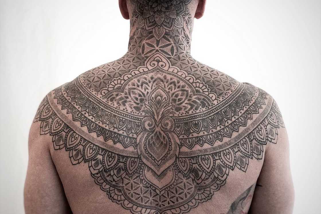A man has a mandala tattoo across his shoulders and back A man has a mandala tattoo across his shoulders and back