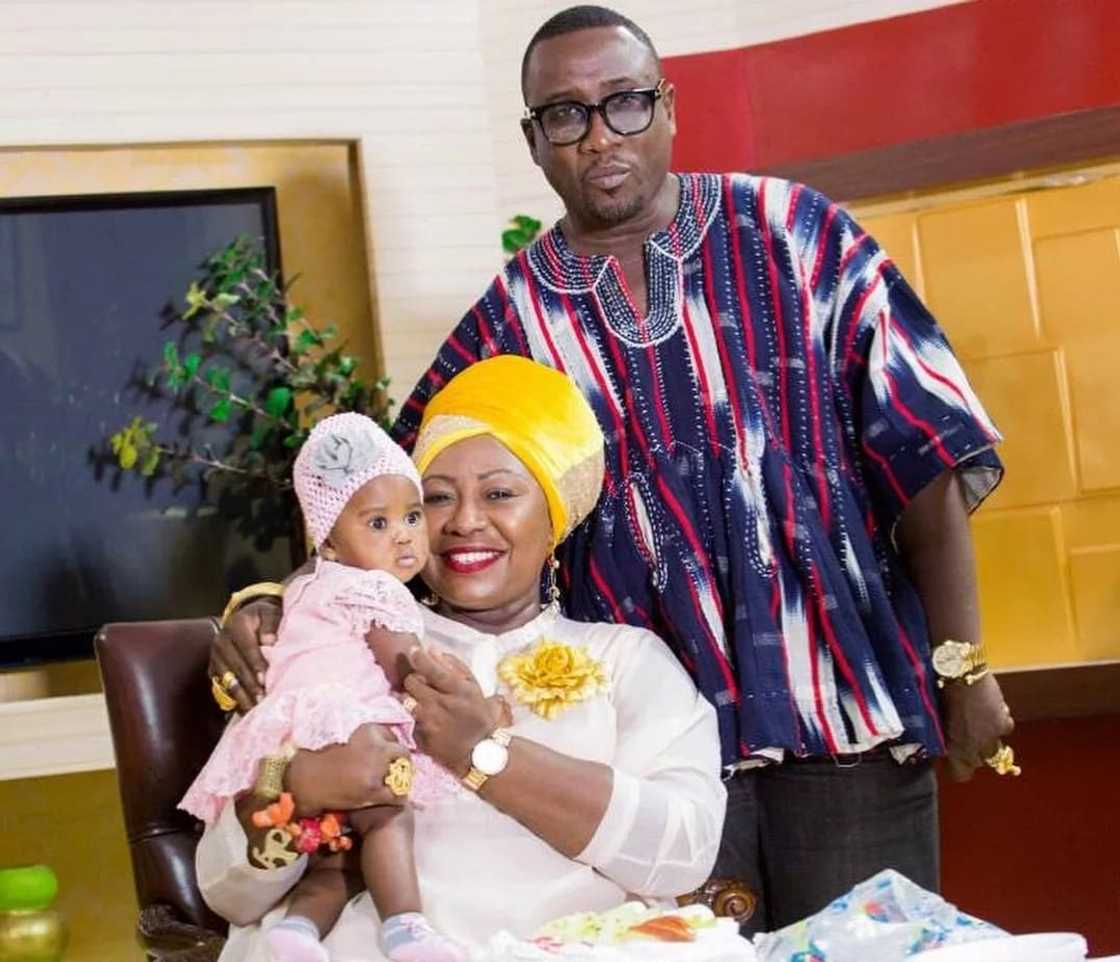 Gifty Anti sits with her baby as her husband stands behind her Gifty Anti sits with her baby as her husband stands behind her