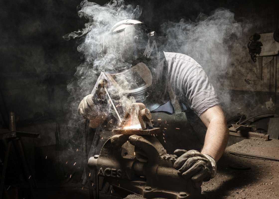 A welder welds metal in a workshop. A welder welds metal in a workshop.