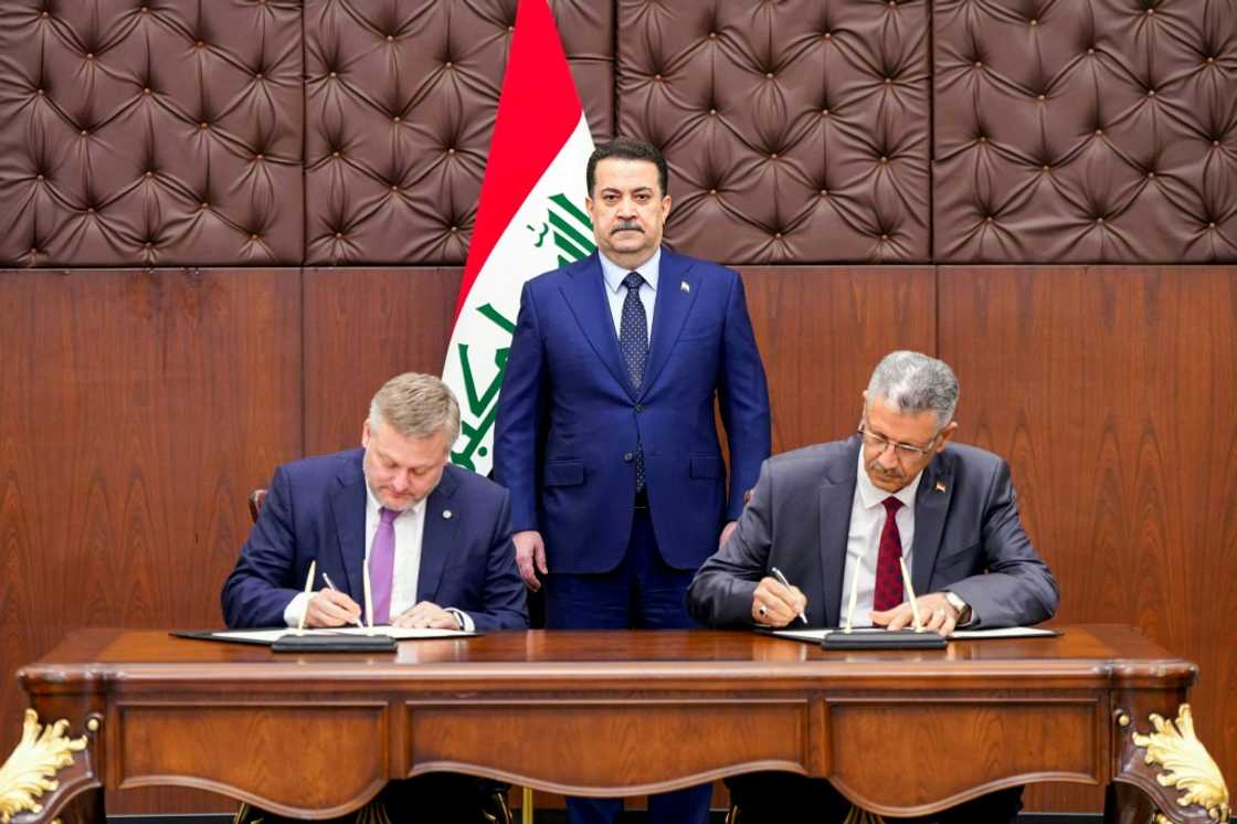 A picture released by the media office of Iraqi Prime Minister Mohamed Shia al-Sudani shows him  looking on as BP CEO, Murray Auchincloss (L) and Iraqi Oil Minister Hayan Abdul Ghani al-Sawad sign a memorandum of understanding to develop oil and gas fields in Kirkuk.