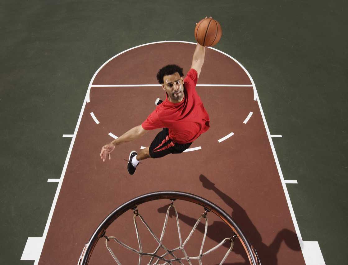 An individual in red attire jumping up to slam dunk a basketball. An individual in red attire jumping up to slam dunk a basketball.