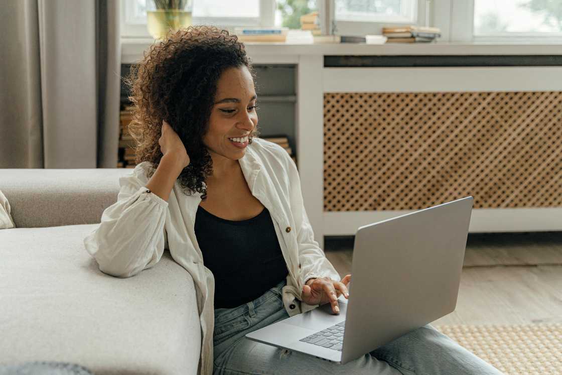 A woman is using a laptop as she sits on the floor