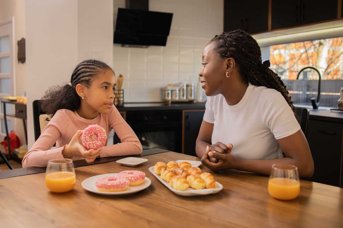 Child in pink shirt holds a donut while sitting at a kitchen table with an adult. Child in pink shirt holds a donut while sitting at a kitchen table with an adult.
