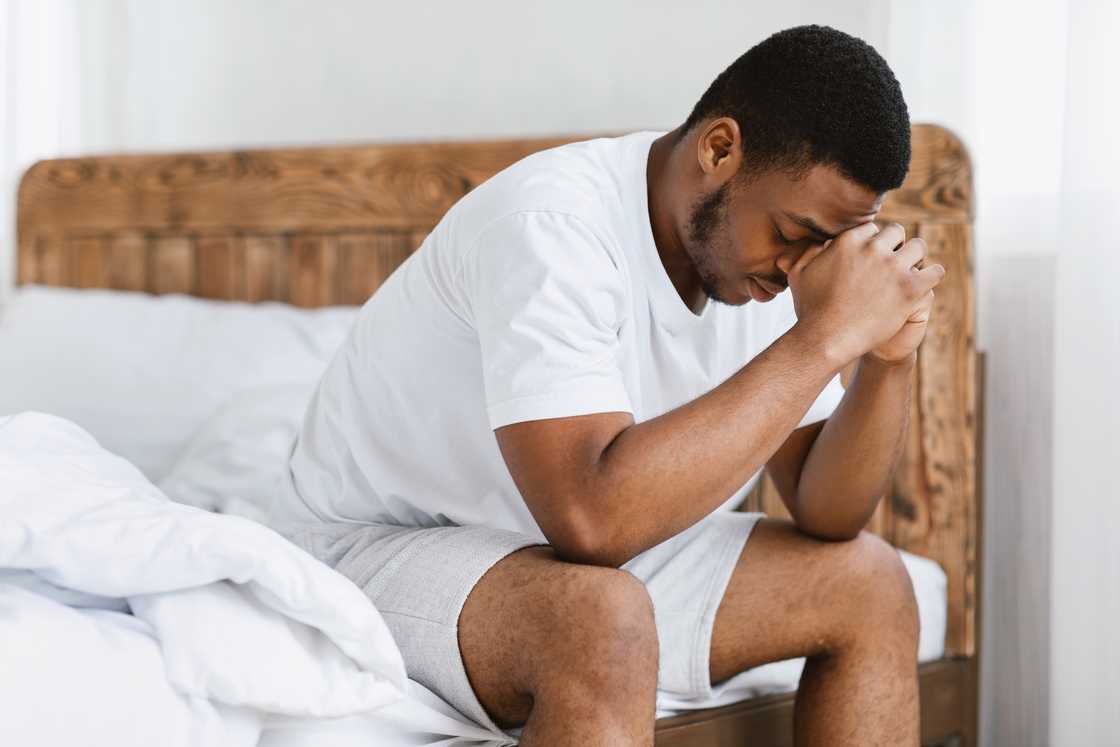 A person sitting on edge of bed in morning sunlight, head in hands.