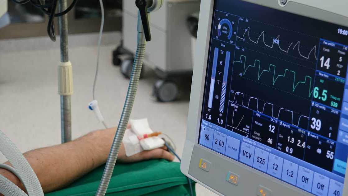 A hospital monitor displays vital signs beside a patient's arm. A hospital monitor displays vital signs beside a patient's arm.