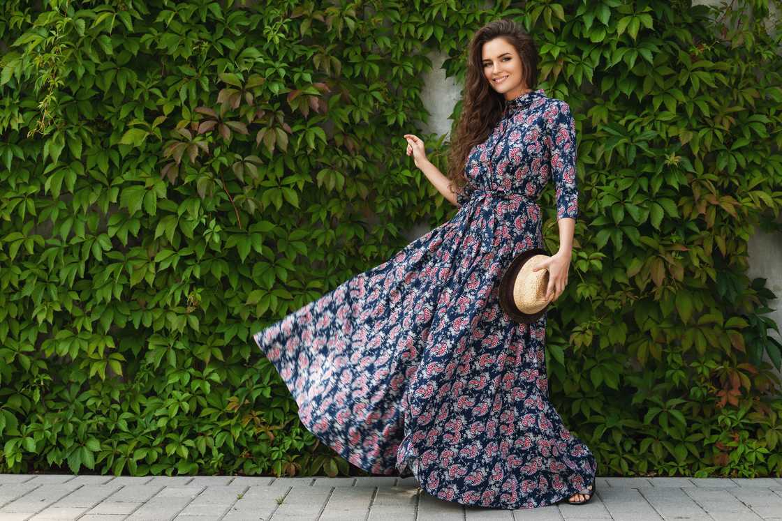 A gorgeous woman wearing a beautiful maxi dress poses against the wall with a wild grape A gorgeous woman wearing a beautiful maxi dress poses against the wall with a wild grape