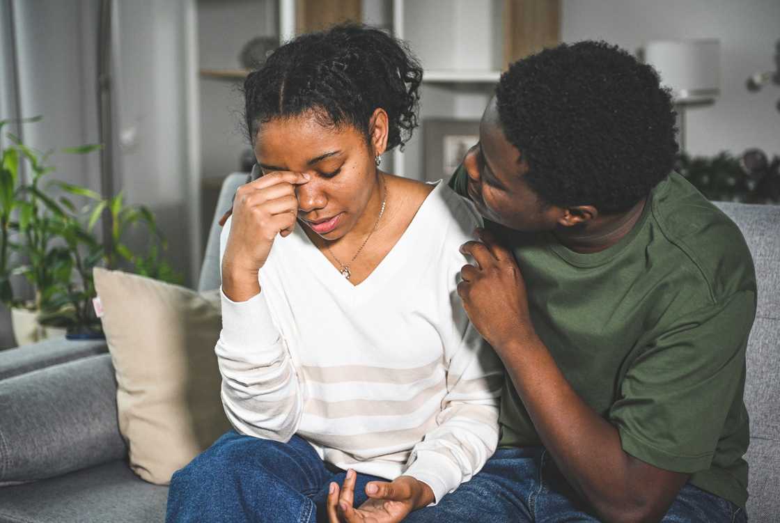 A woman crying on a friend's couch while he consoles her.