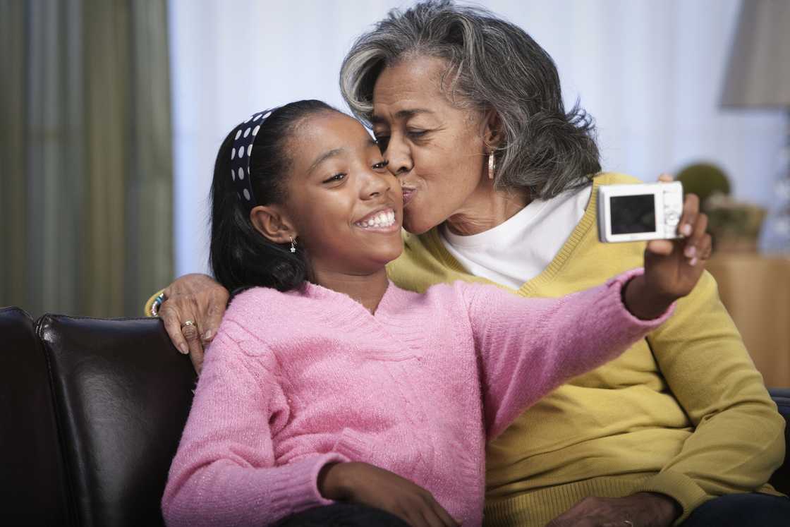 Older woman kisses young girl as she takes a selfie.