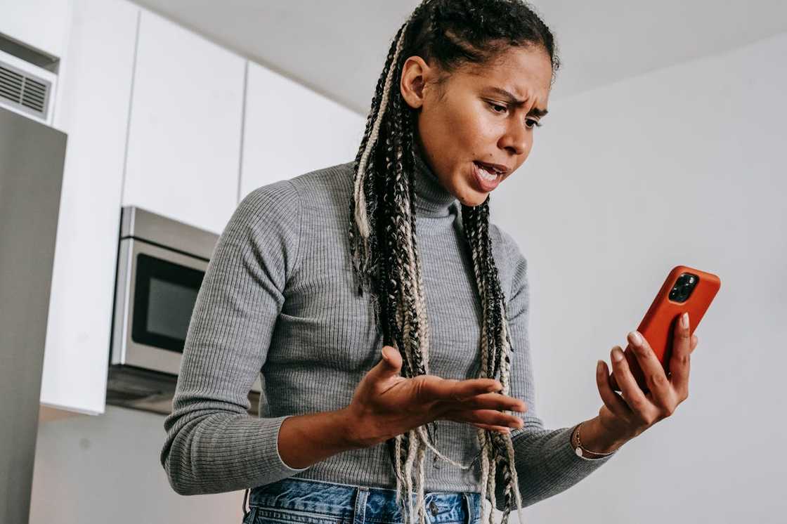 Upset woman with braided hair looking at her phone indoors.