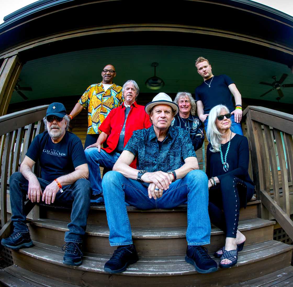 Group photo of the Wet Willie Band sitting and standing on a wooden porch, featuring seven members in casual attire, showcasing the legendary Southern rock group.