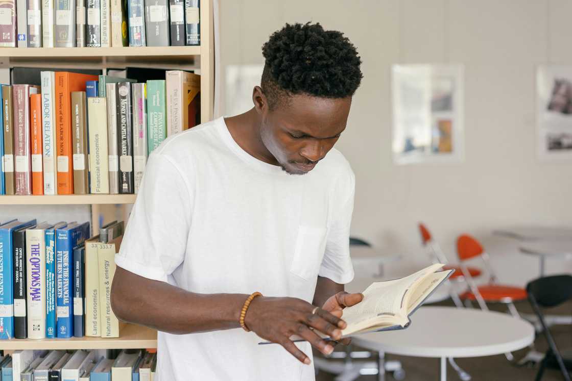 A man in a white shirt is reading a book in a library