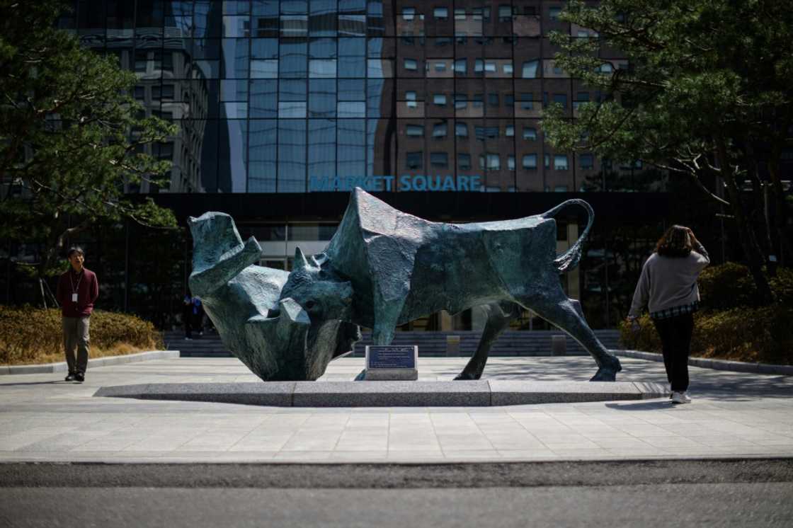 People walk past a bull and bear sculpture in front of the Korea Exchange building in Seoul