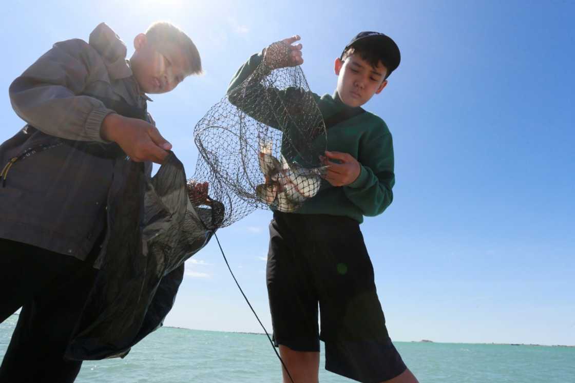 Boys fish near a copper plant which is discharging industrial waste into a body of water right next to the lake