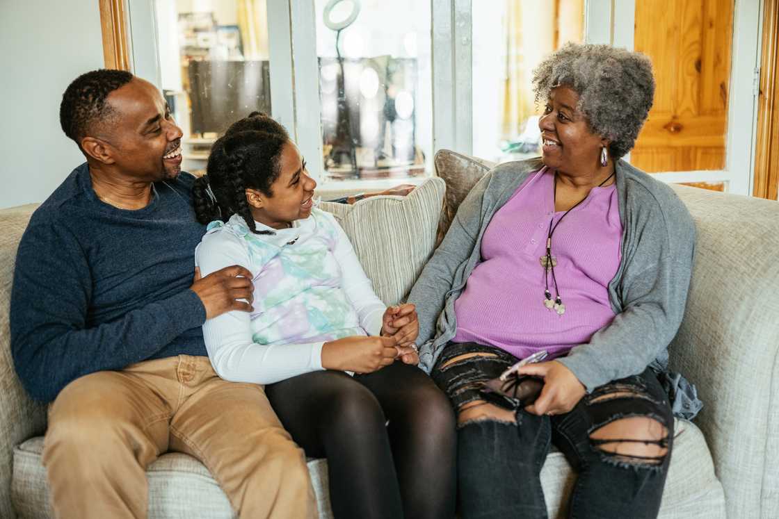 Three people sit close together on a beige couch, smiling and making eye contact.