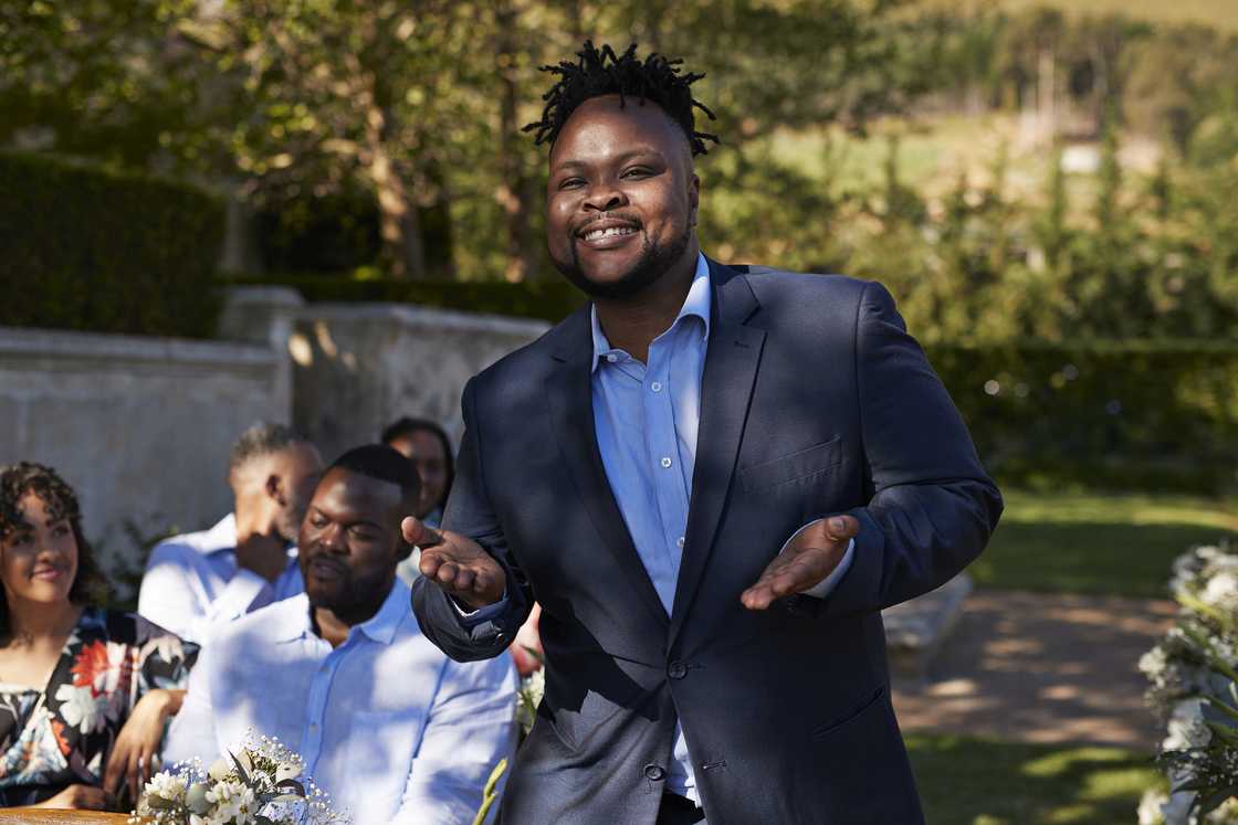A smiling man in formals gesturing during ceremony.