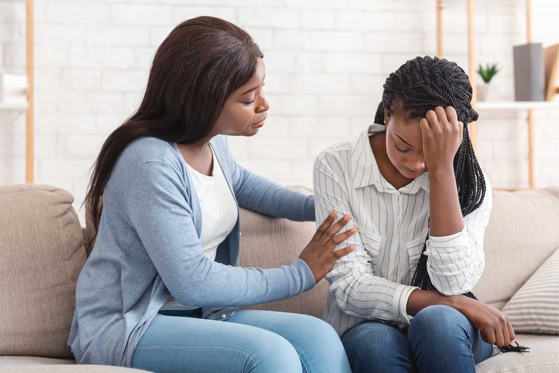 A woman supporting her depressed friend sitting on sofa