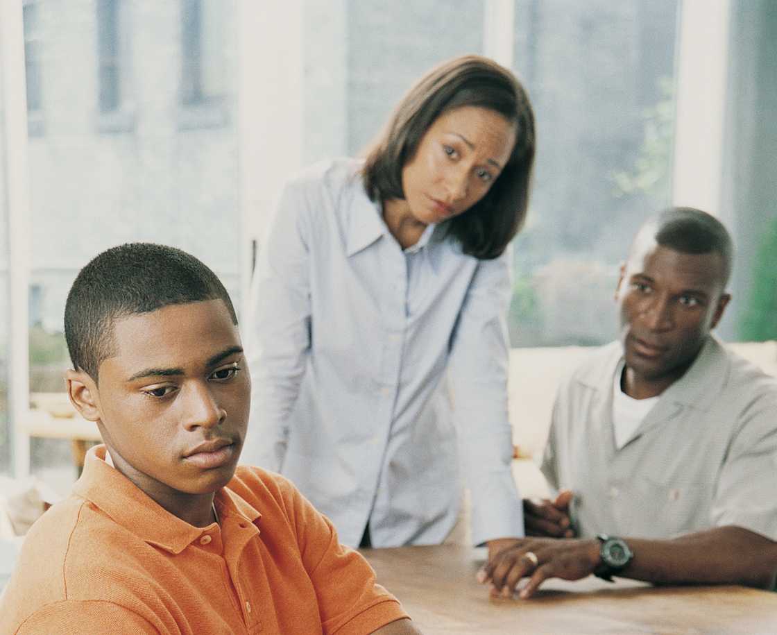 Young person sits quietly while two adults look on with concern.
