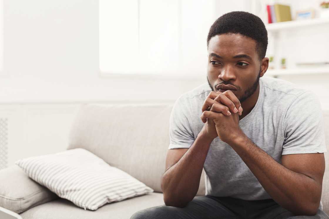 A man with hands clasped thinking while sitting on couch