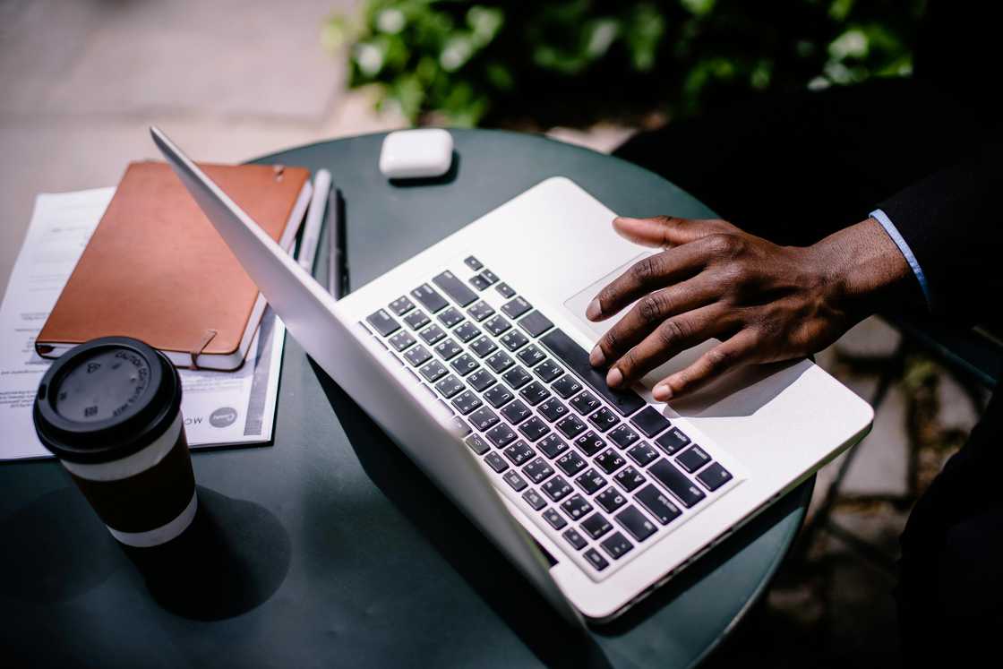 A hand is pictured using a laptop on a black coffee table A hand is pictured using a laptop on a black coffee table
