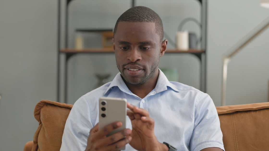 A man using his phone while sitting on sofa at home A man using his phone while sitting on sofa at home