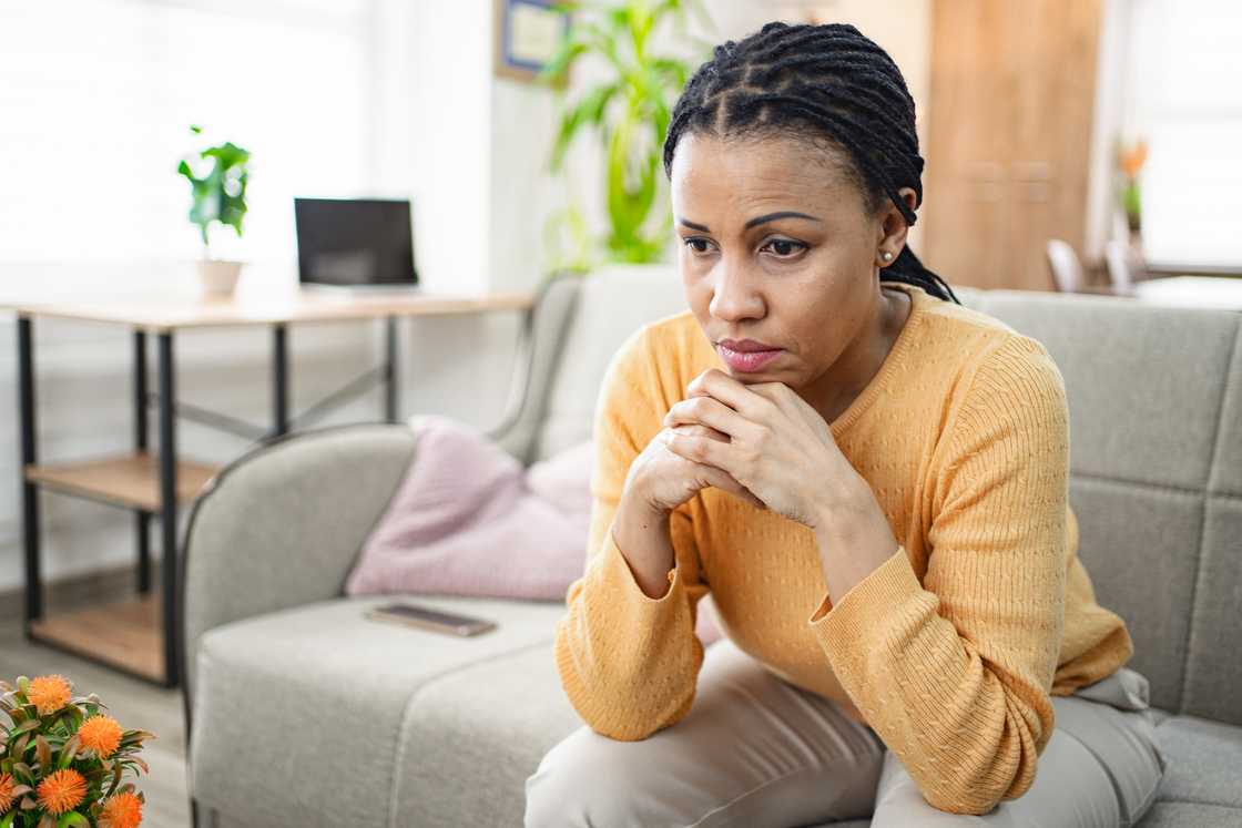 A black woman thinking while sitting on a sofa at home