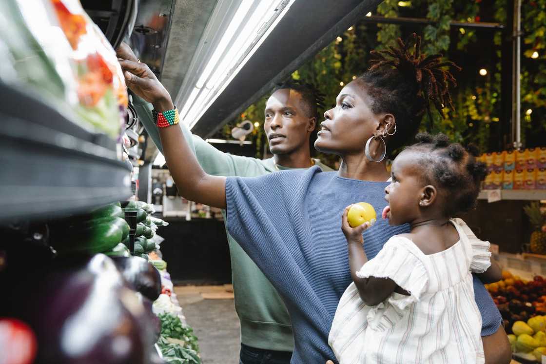 A woman holding a small child shops for produce while a man stands besides her. A woman holding a small child shops for produce while a man stands besides her.