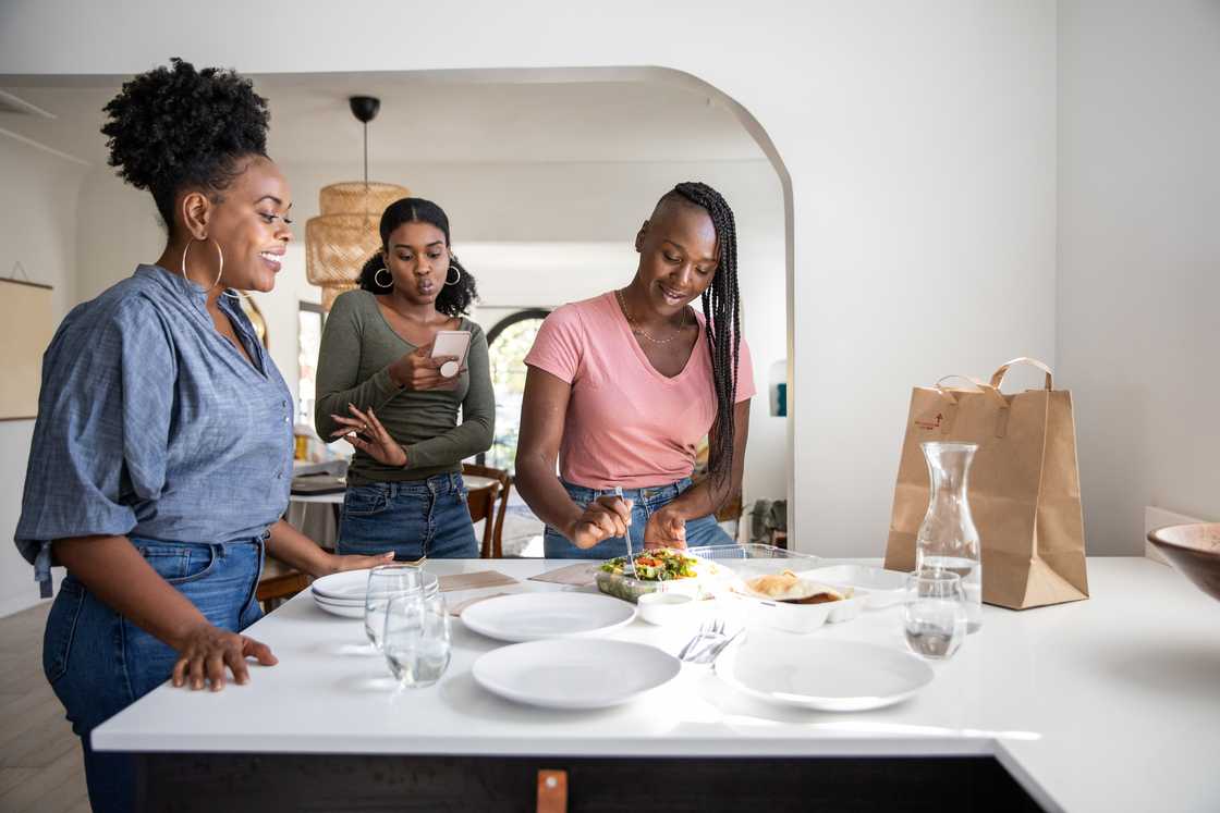 Three people gather in a modern kitchen, chatting and preparing food.