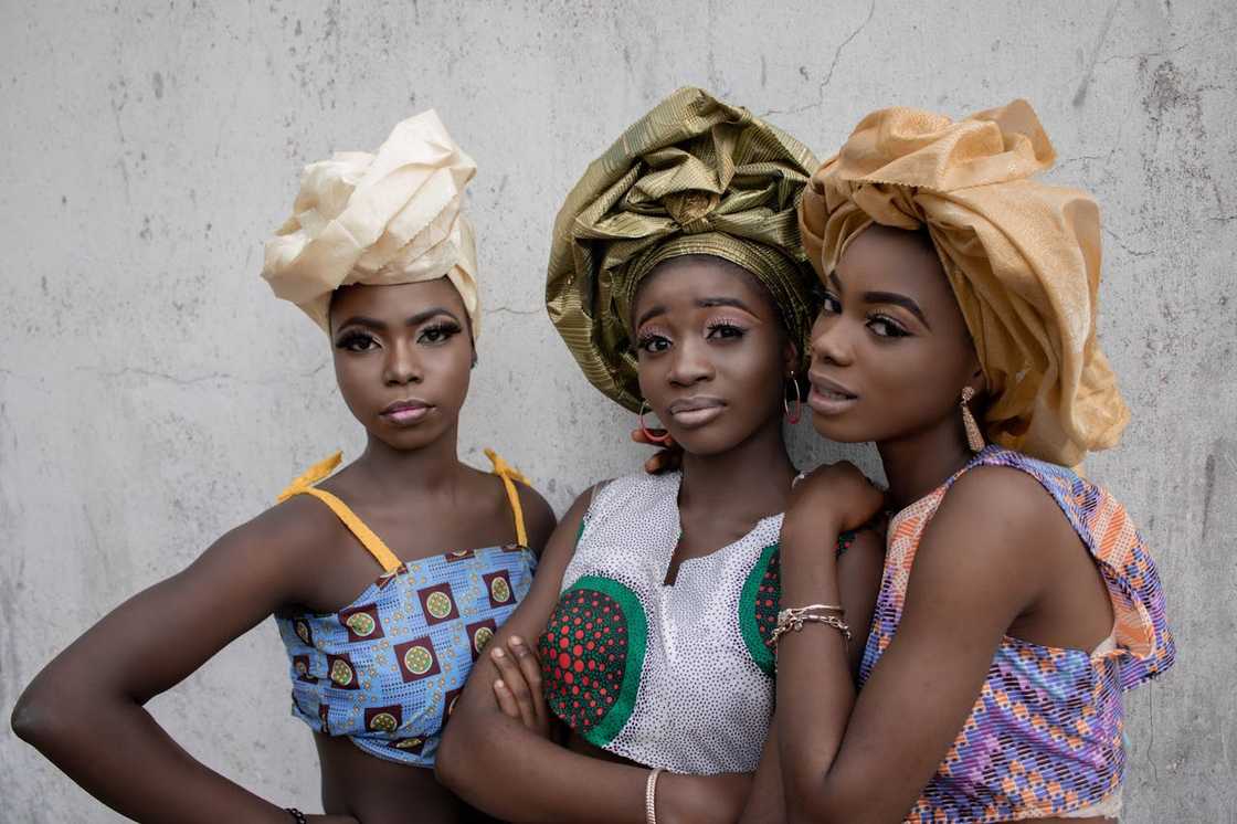 Three women wearing traditional headwraps pose together.