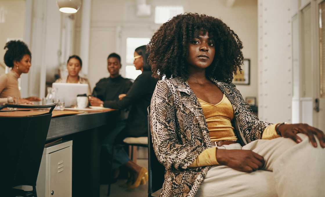 Person sits confidently in foreground while others collaborate in a bright office.