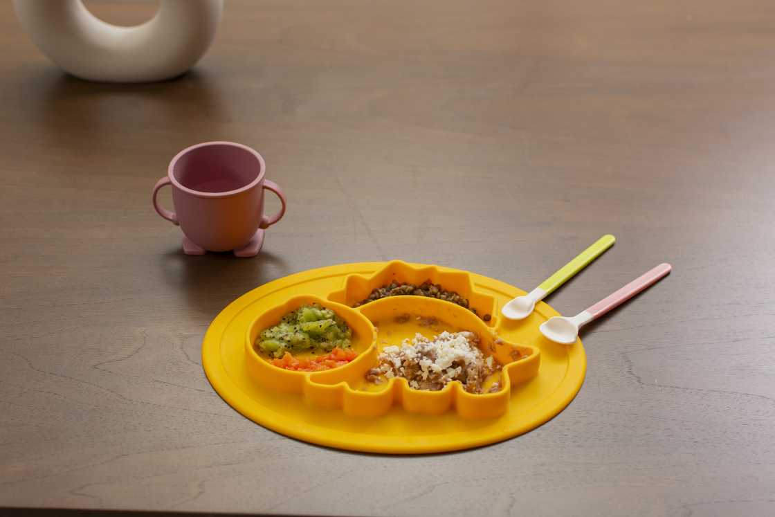 Baby's food in a plate and a cup besides it